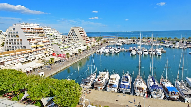 A marina with numerous boats docked, a large cruise ship, and modern buildings with balconies. - Renovated Boho Studio ☀ Pool | Beach | Queen-size bed (La Grande Motte)