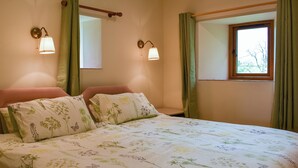 A bedroom with a floral bedspread, two wall-mounted lamps, a window with curtains, and a wooden headboard.