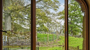 A rustic wooden gate leading to a stone wall and a grassy area with trees.