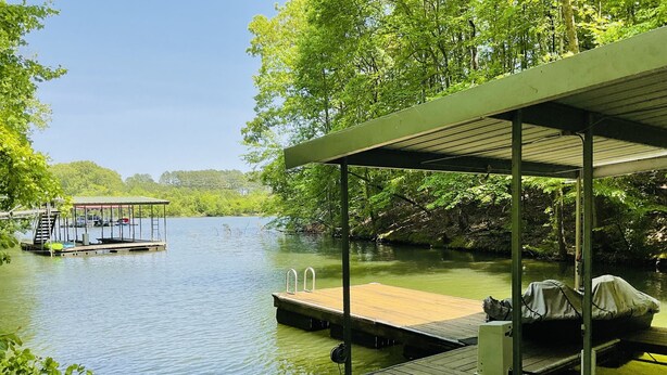 A wooden dock extending into a calm river, with a covered seating area and a boat covered with a tarp. - Family friendly lake front home with private dock in a cove (Winchester)