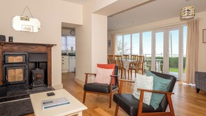 A spacious living room with a fireplace, wooden flooring, and a view of the outdoors through large windows. - An eco-friendly holiday bungalow near Abererch Beach on the Llyn Peninsula. (Pwllheli)