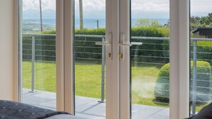 A bedroom with a large sliding glass door leading to a balcony with a view of the sea and greenery. - An eco-friendly holiday bungalow near Abererch Beach on the Llyn Peninsula. (Pwllheli)
