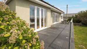 A modern building with a flat roof, large glass doors, and a paved deck. - An eco-friendly holiday bungalow near Abererch Beach on the Llyn Peninsula. (Pwllheli)