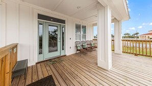 A covered porch with a wooden deck, a sliding glass door, and a seating area with chairs. - Orange Beach, 4 Master Suites, short drive to Beach. Walk to Zekes and SweetCone (Orange Beach)
