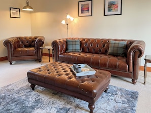 Ein Wohnzimmer mit braunem Ledersofa, passendem Hocker und einem kleinen Beistelltisch.