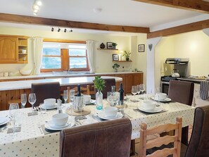 A dining area with a table set for a meal, wooden cabinets, a kitchen with a stove, and a window with curtains.