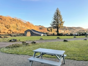A picnic table in a grassy field with a stone bridge and a mountain in the background.