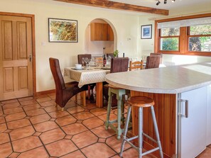 Uma área de refeições com uma mesa redonda, cadeiras, um banquinho de bar, uma cozinha com armários e uma porta.