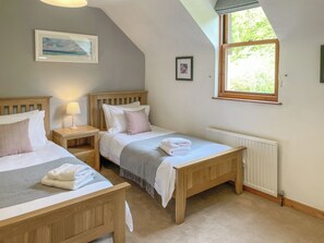 A bedroom with two wooden beds, a window with a view, a radiator, and a framed picture on the wall.