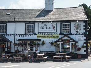 Un pub tradicional con un letrero que dice "The Old Stay", con mesas al aire libre y macetas colgantes de flores.
