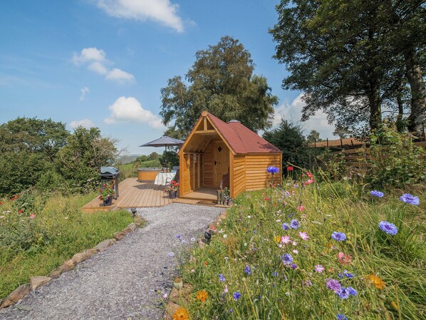 Una cabaña de madera con techo rojo, un jacuzzi y una mesa con sillas afuera.