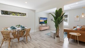 A modern living room with a dining area, a large potted plant, a TV, and a sofa. - Beach Don't Kill My Vibe by Beach Boutique Rentals (Anna Maria)
