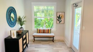A room with a wooden bench, a black cabinet with a mirror, a window with a view of greenery, and a door with a screen. - Beach Don't Kill My Vibe by Beach Boutique Rentals (Anna Maria)