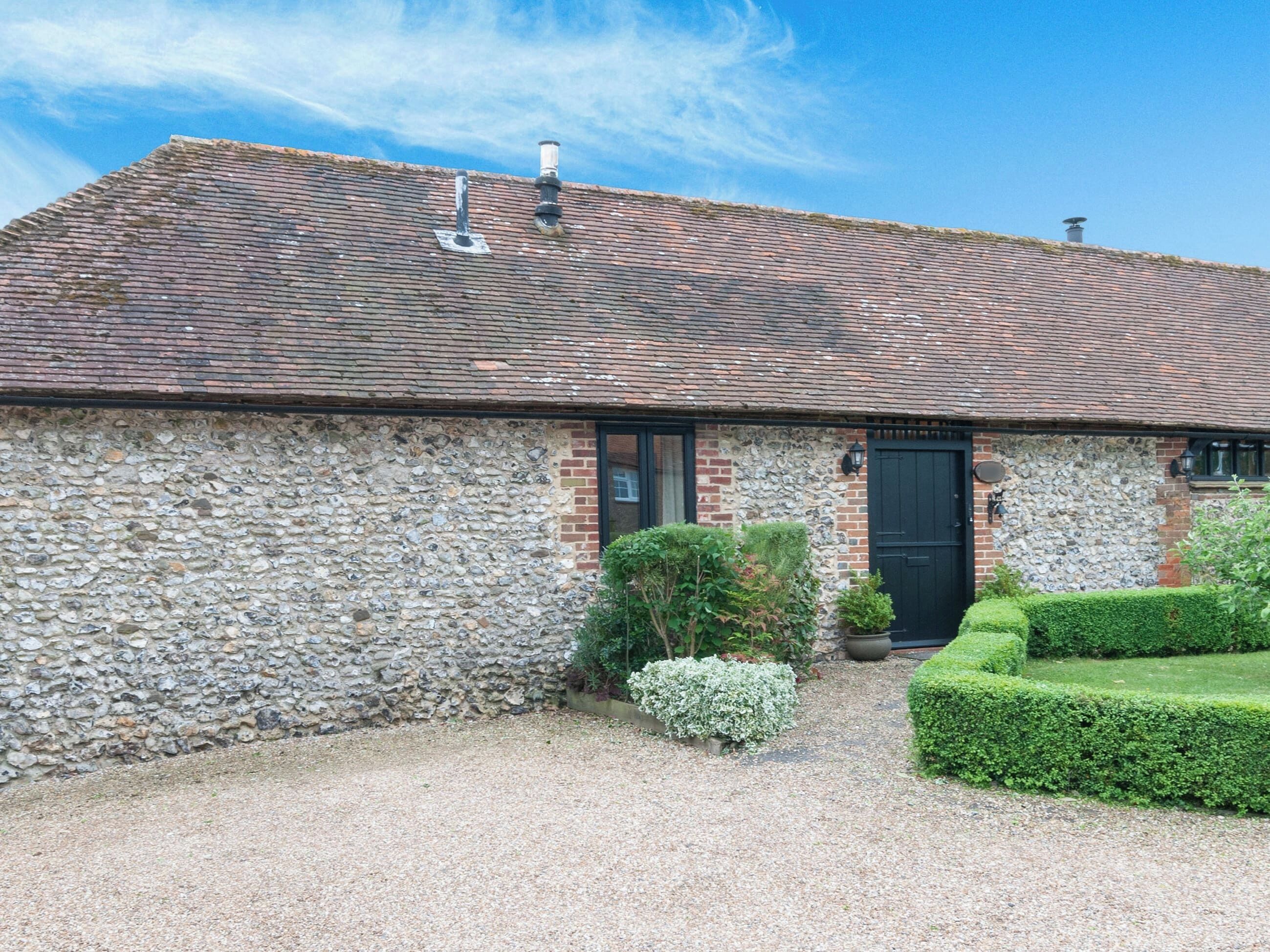 A stone building with a tiled roof, a black door, and a gravel driveway.