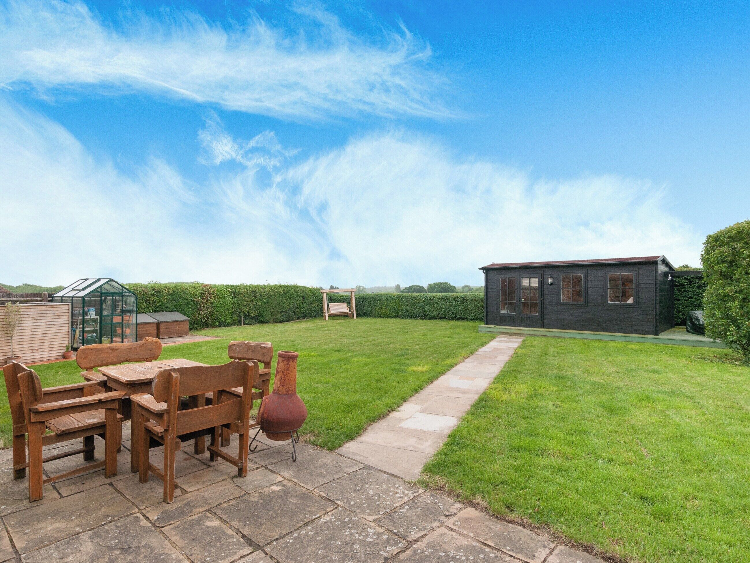 A backyard with a wooden table and chairs, a small shed, and a house.