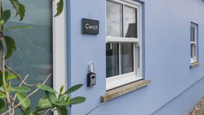 Un edificio con fachada azul, una puerta y un ventanal con una placa que dice 'Cwtch'.