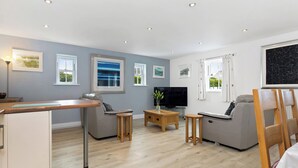 Una sala de estar moderna con un televisor de pantalla plana, sofás grises, una mesa de centro de madera y obras de arte en las paredes.