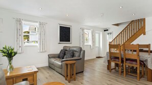 Una sala de estar moderna con un sofá, una mesa de madera, una escalera y una ventana con cortinas.