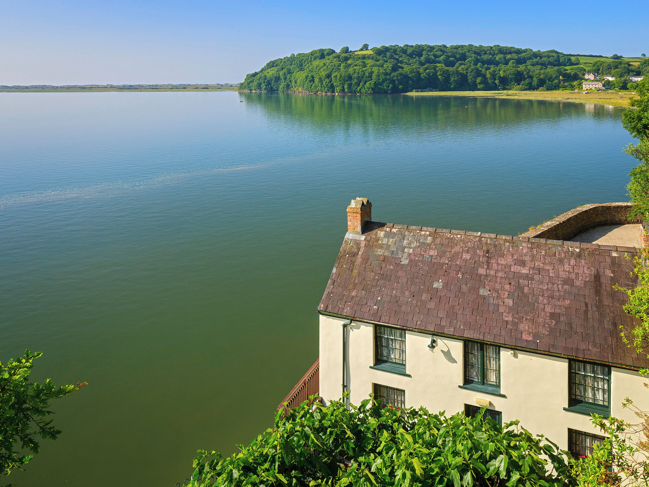A riverside view with a building featuring a brick roof and multiple windows.