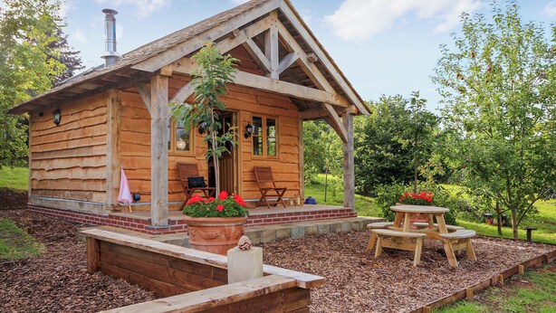 A wooden cabin with a porch, outdoor seating, and a garden area. - 1 bedroom accommodation in Malpas (Malpas)