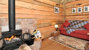 A cozy log cabin interior with a fireplace, a red sofa, and a wooden ceiling. - 1 bedroom accommodation in Malpas (Malpas)
