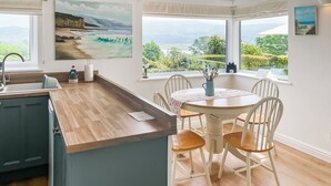 A kitchen with a wooden countertop, a dining table with chairs, and large windows with a view of greenery and mountains. - 2 bedroom accommodation in Portmeirion (Portmeirion)