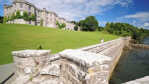 A historic building with a large lawn and a stone wall by a body of water. - 2 bedroom accommodation in Portmeirion (Portmeirion)