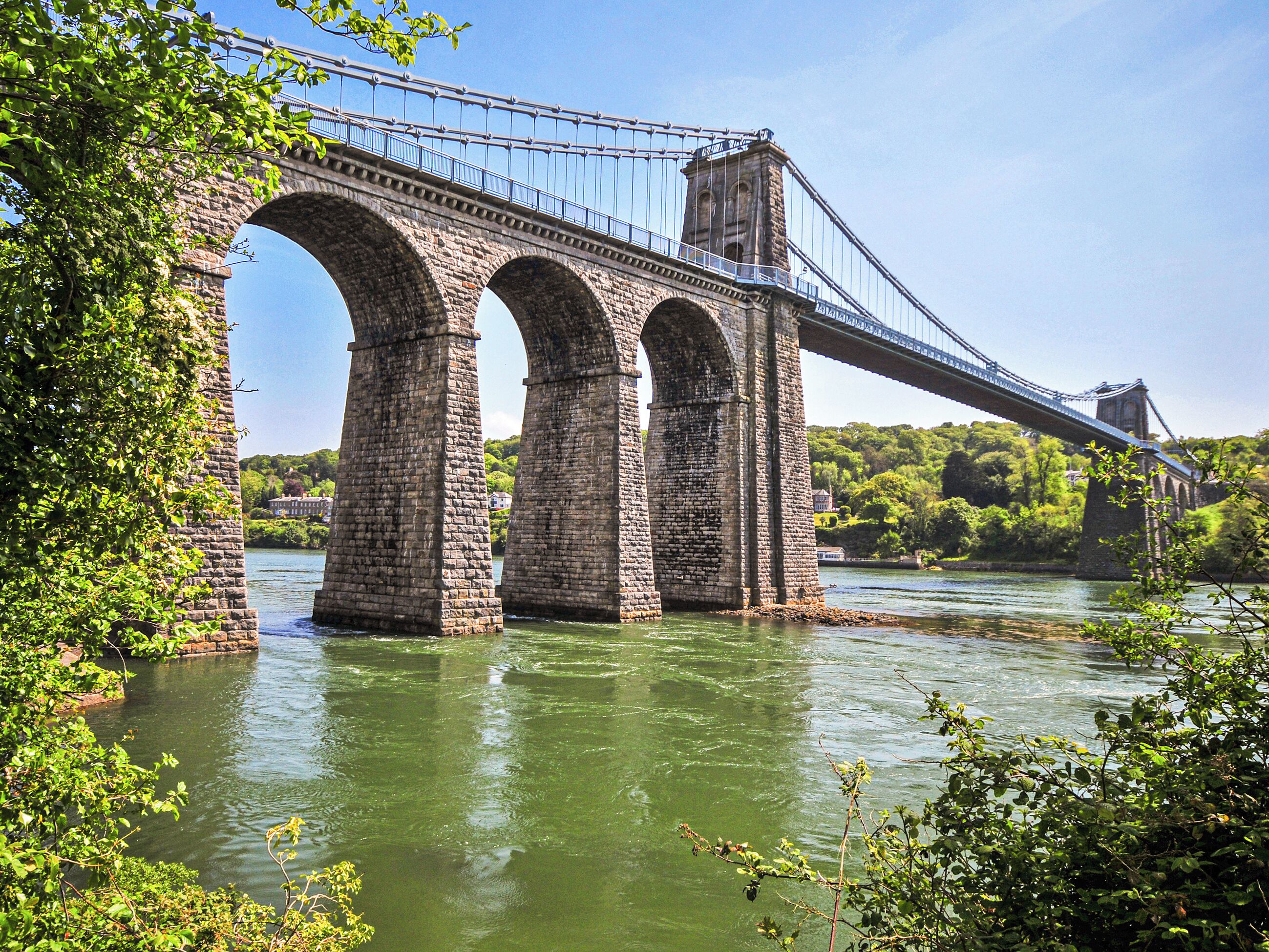 Uma ponte de pedra com várias arcadas sobre um rio, rodeada por vegetação.