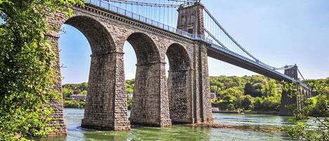 Uma ponte de pedra com várias arcadas sobre um rio, rodeada por vegetação.