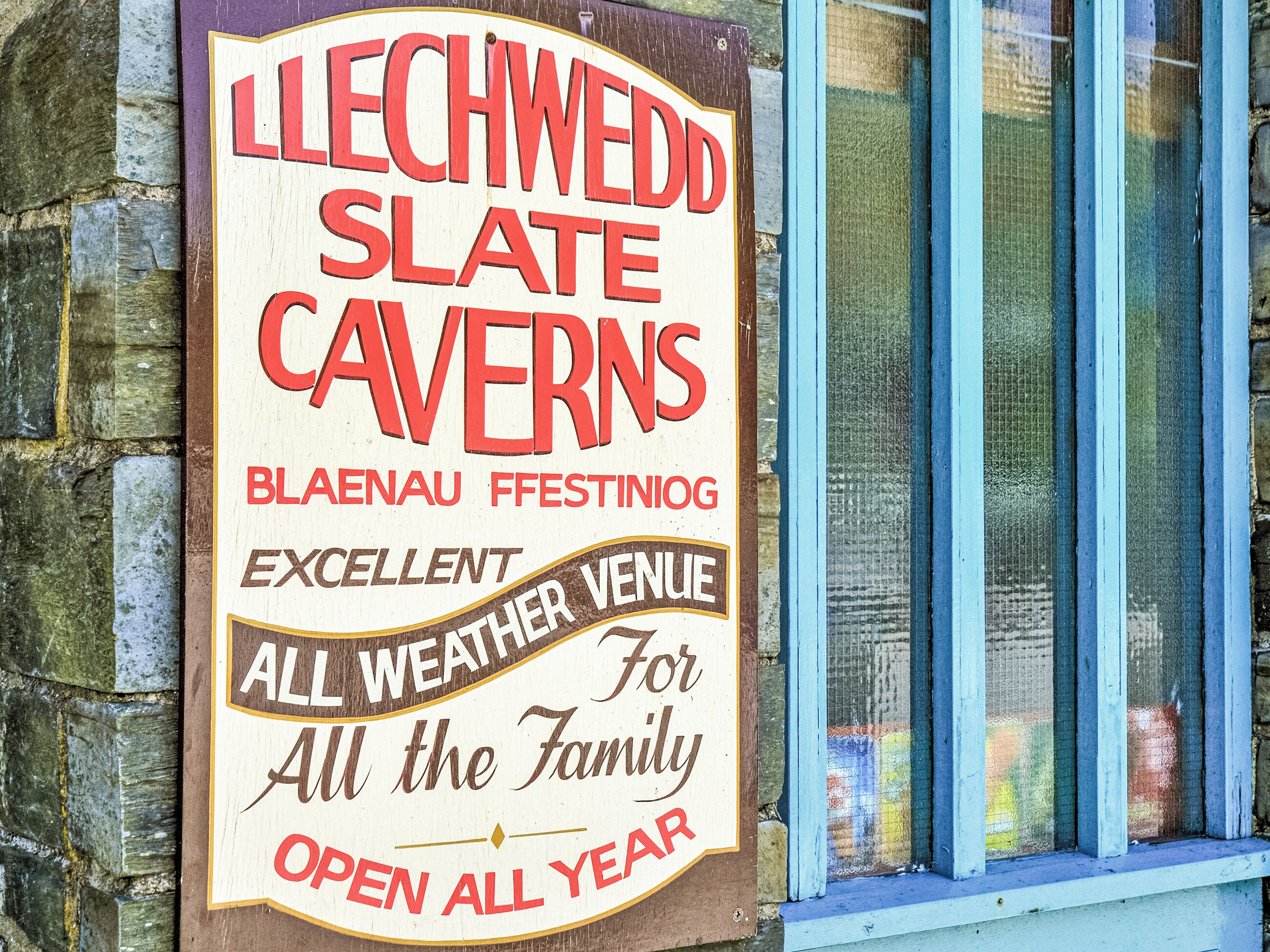 A sign for Llechwedd Slate Caverns advertising 'Blaenau Ffestiniog' and 'EXCELLENT ALL WEATHER VENUE FOR ALL the Family OPEN ALL YEAR.'