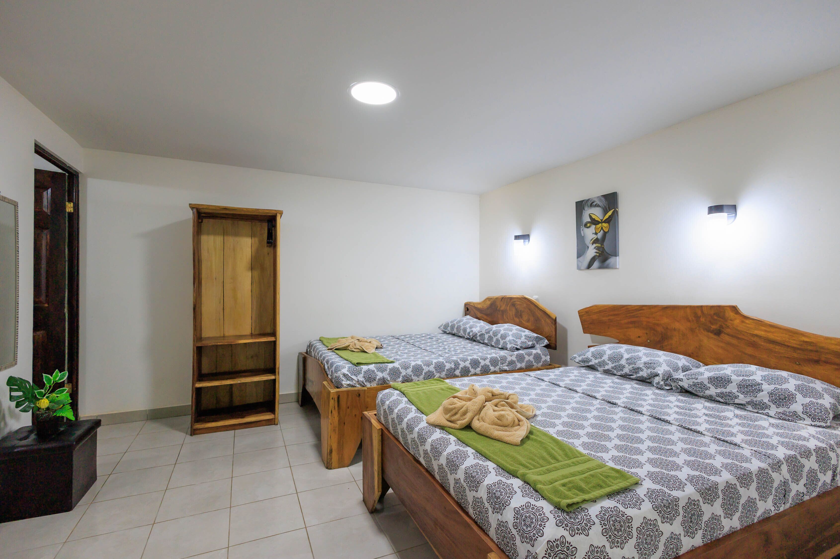 A room with two wooden beds, a wooden wardrobe, a potted plant, and a painting on the wall.