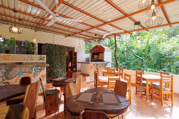 An indoor dining area with wooden furniture and a view of lush greenery outside. - Hotel Boutique D Angelo (Manzanillo)