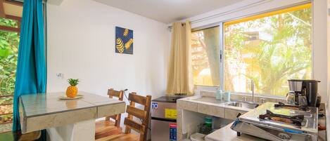 A compact kitchen with a refrigerator, a stove, and a window with curtains.