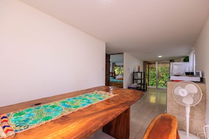 Una habitación con una mesa de madera, un ventilador y vistas a un balcón con plantas.