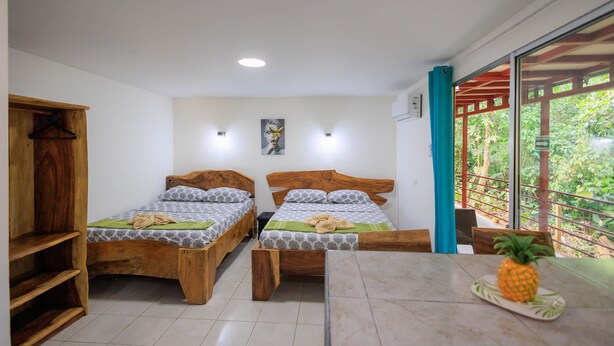 Een kamer met twee houten bedden, een tafel met een ananas, en uitzicht op groen door een raam.