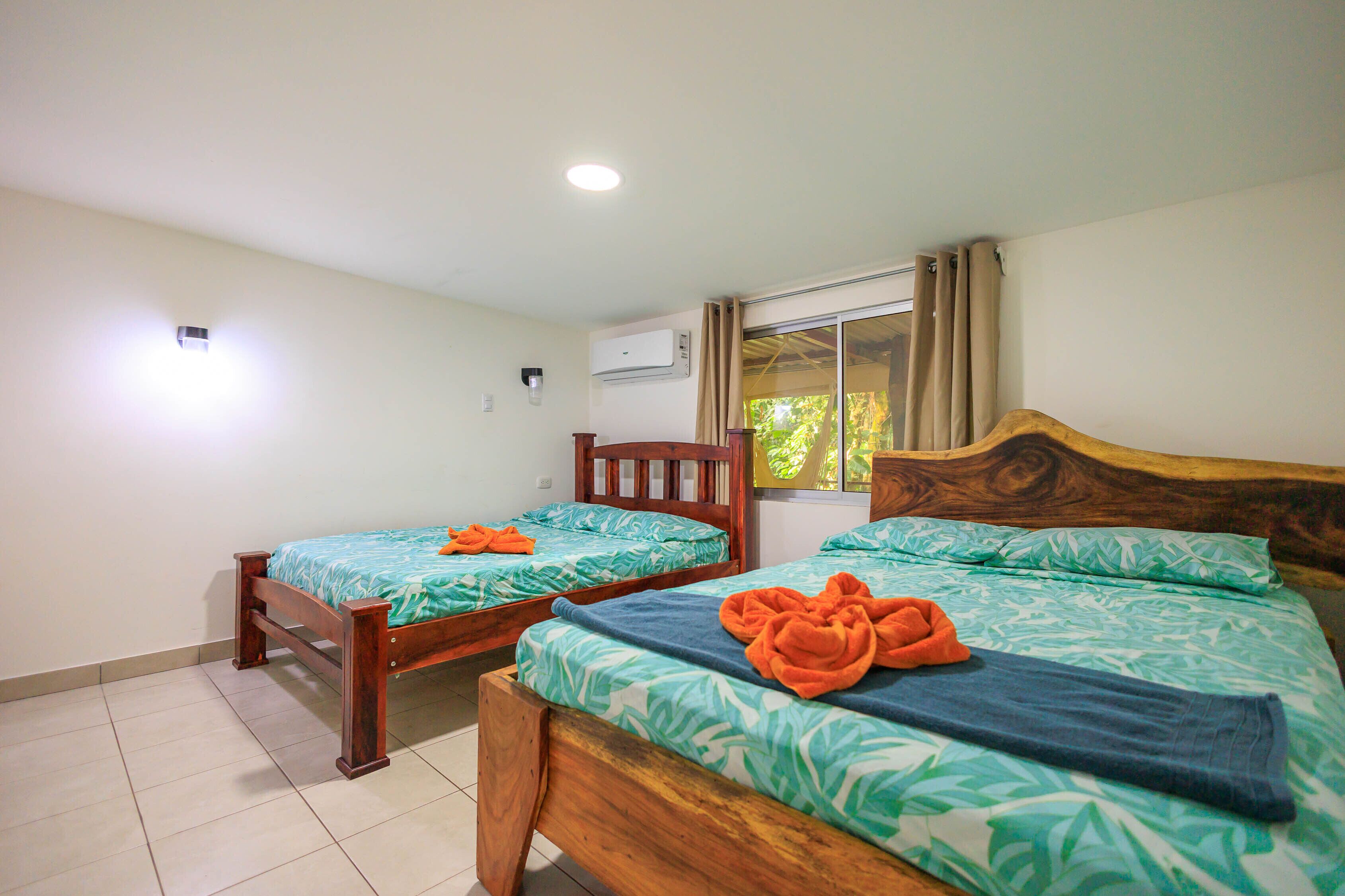 A room with two wooden beds, each with a green leaf-patterned bedspread and orange towels.