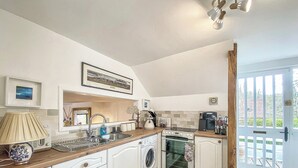 Cocina compacta con muebles blancos, horno empotrado, lavadora y encimera de madera.