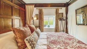 Un dormitorio con una cama grande, una ventana con cortinas, una lámpara y una planta en el alféizar.