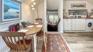 Un comedor con una mesa y sillas de madera, un cuadro grande en la pared y vistas a la cocina.