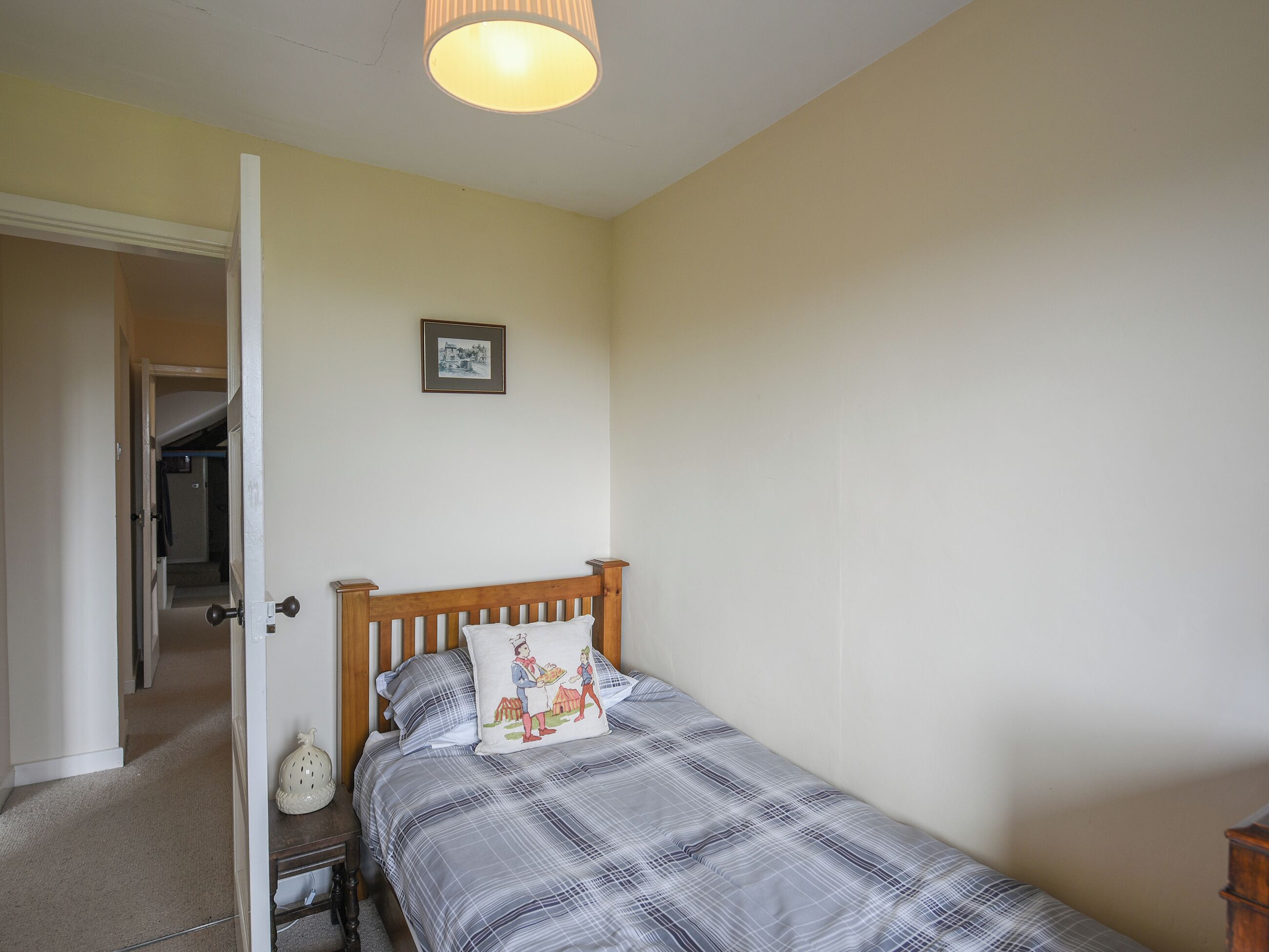 Un dormitorio con una cama de madera, una puerta blanca, un cuadro enmarcado en la pared y un pasillo que conduce a otra habitación.