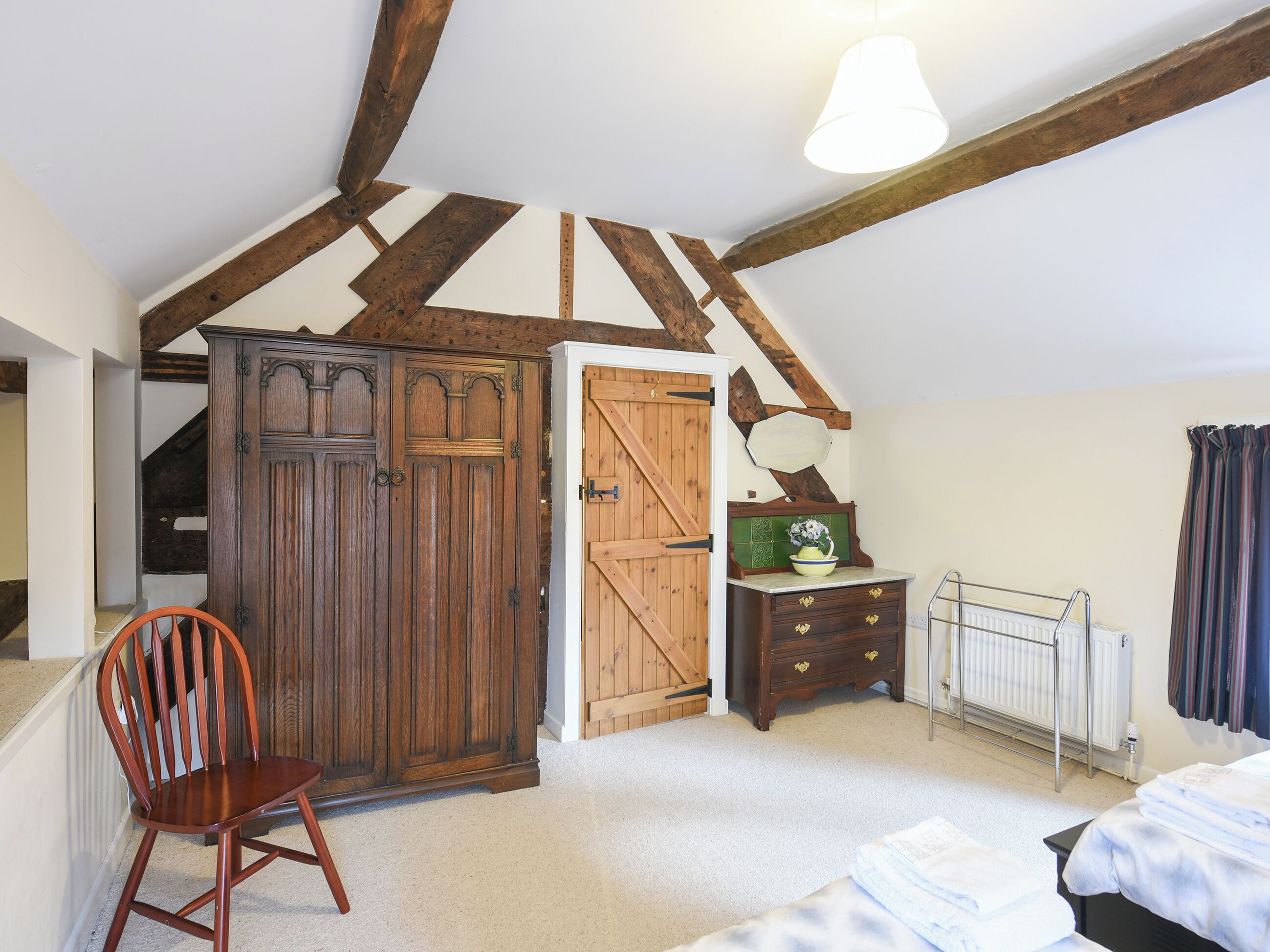 Een slaapkamer met zichtbare houten balken, een garderobe, een dressoir, een radiator en een stoel.