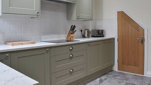 Une cuisine avec des meubles de couleur vert clair, un plan de travail blanc et une porte en bois.