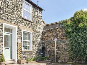 A stone building with a door and windows, a sign indicating resident parking, and a small garden area with flowers.