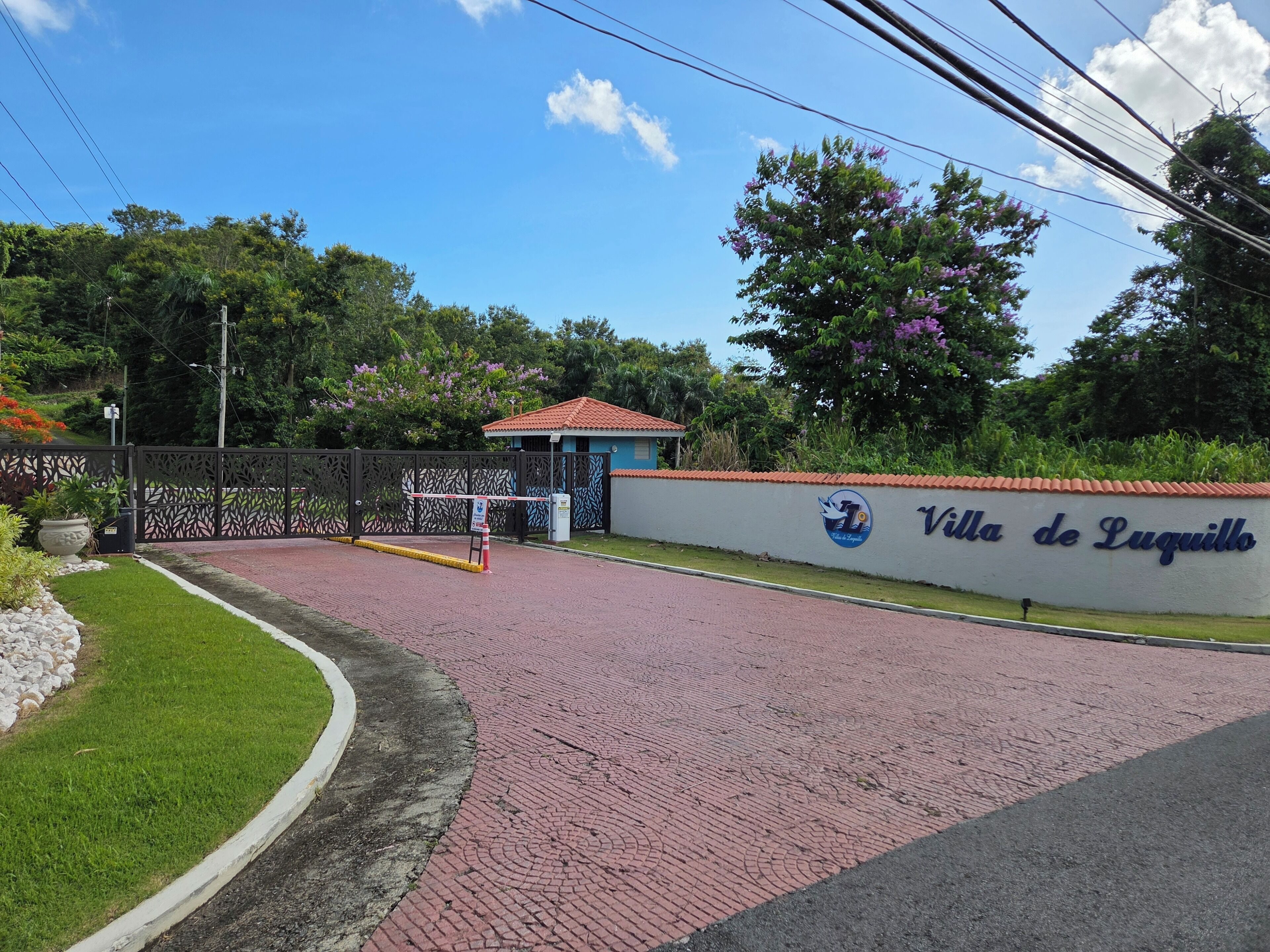 A gated entrance with a sign reading 'Villa de Luquillo' and a small building with a red roof.