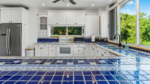 A modern kitchen with white cabinets, a stainless steel refrigerator, a built-in oven, and a large window offering a view of greenery. - Your Private Slice of Paradise! (Luquillo)