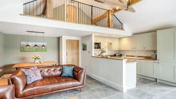 Un vaste espace de vie comprenant un canapé en cuir marron, une table basse en bois et une cuisine dotée de meubles blancs et d’un îlot central.