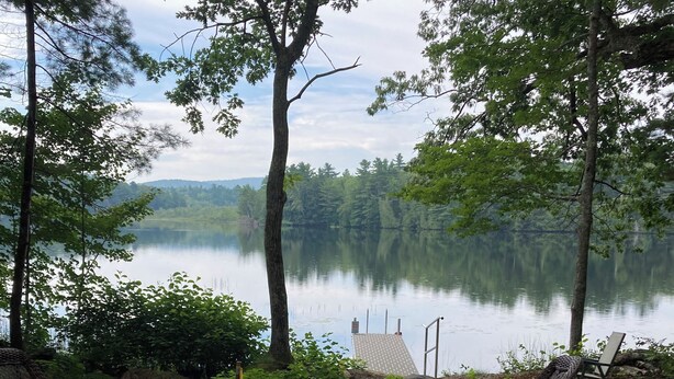 A deck with wicker furniture overlooking a lake, surrounded by trees. - Studio Apartment on lake near Camden, Maine. (Lincolnville)