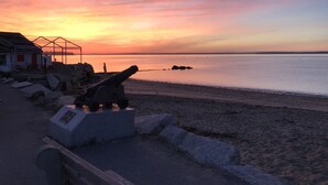 A coastal scene with a cannon on a concrete base, a wooden structure, and a calm sea at sunset. - Studio Apartment on lake near Camden, Maine. (Lincolnville)