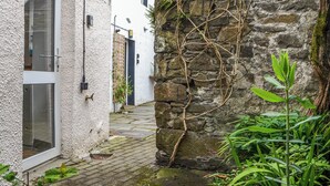 A narrow stone pathway leading to a white building with a glass door. - 1 bedroom accommodation in Keswick (Keswick)