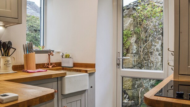 A kitchen with wooden countertops, a sink, and a window overlooking a stone wall and greenery. - 1 bedroom accommodation in Keswick (Keswick)